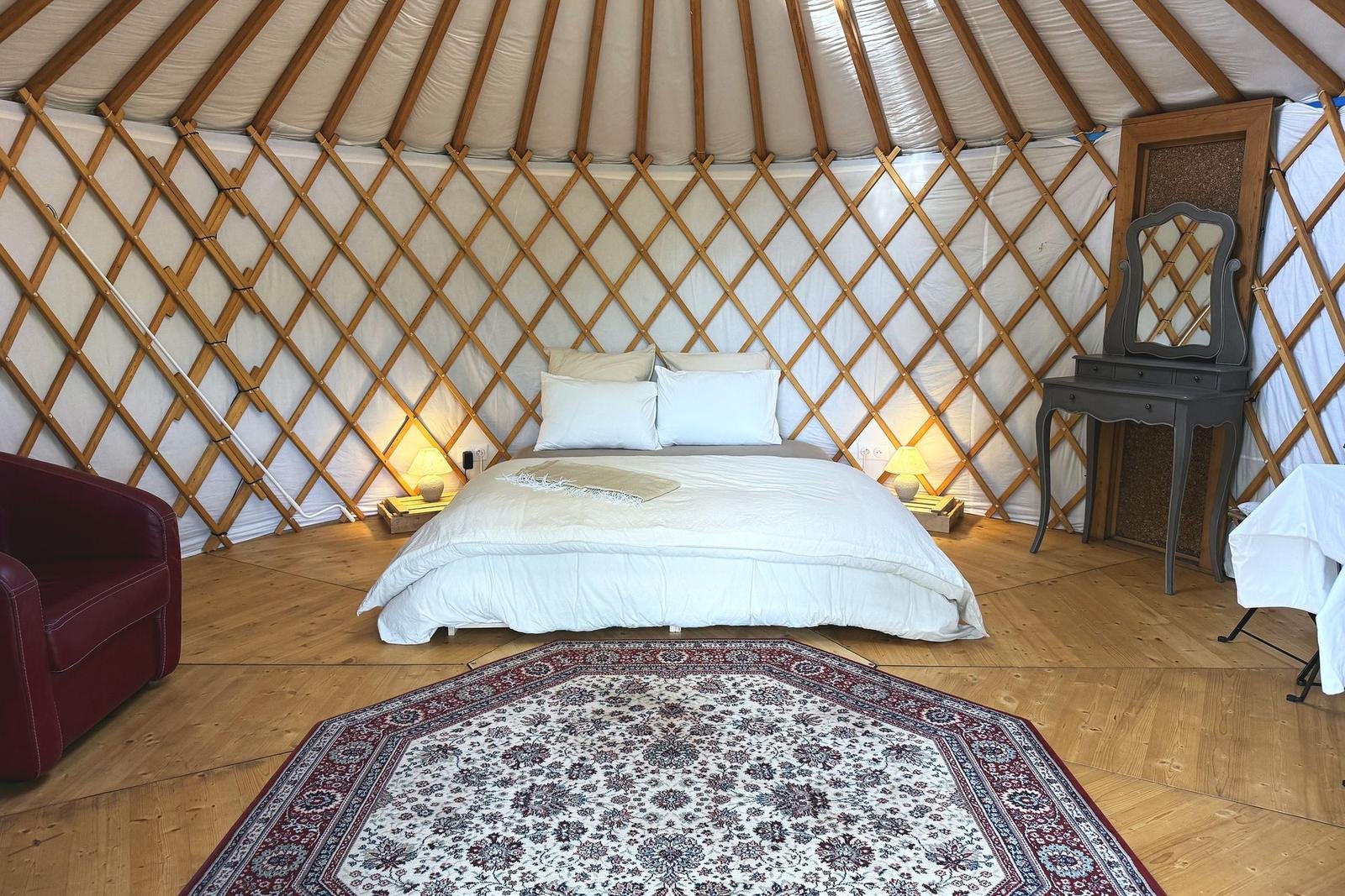 Intérieur de la yourte : lit double fait, lampes allumées, treillis de bois et tapis