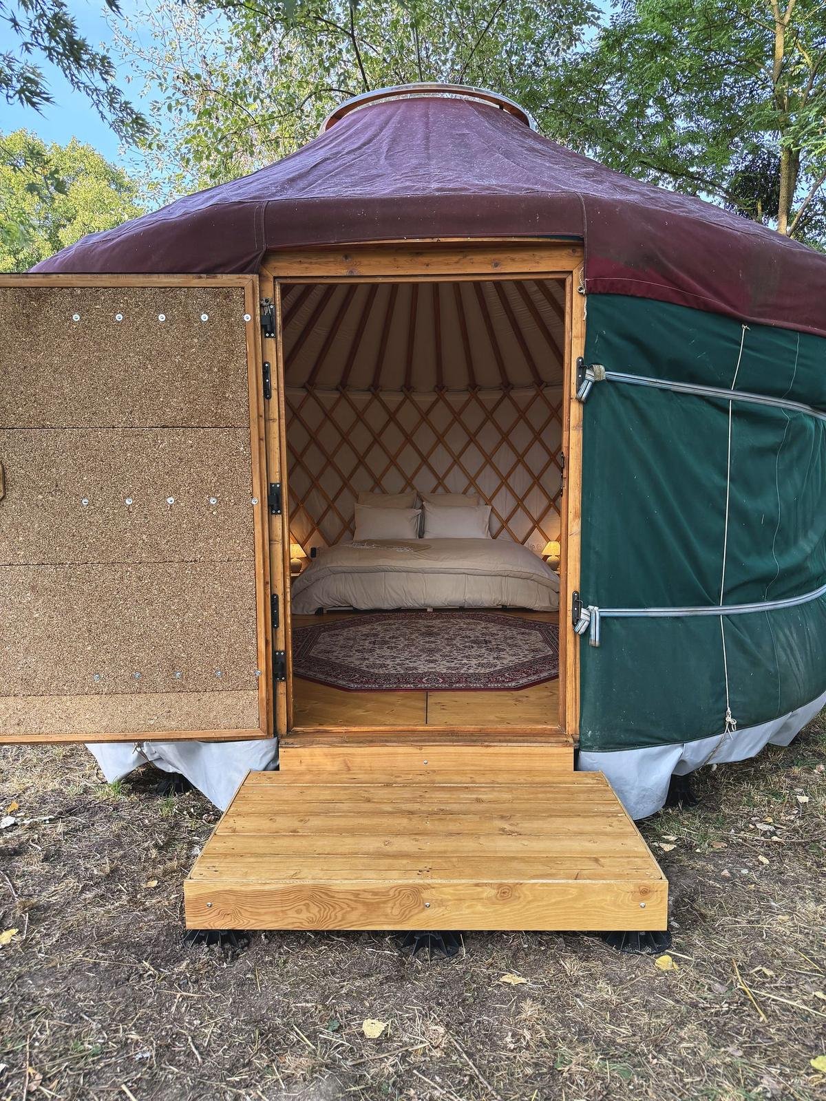 Porte de la yourte ouverte sur le lit, marche en bois devant l’entrée
